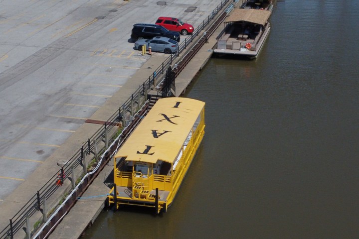 Yellow water taxi docked along a pier beside parked cars.