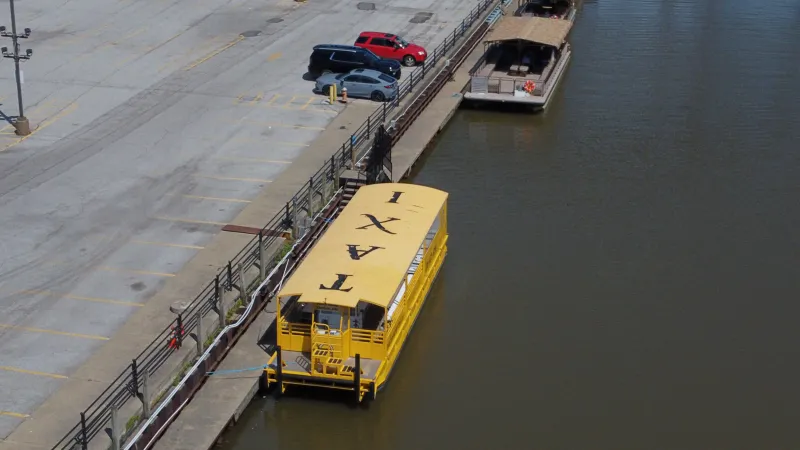 Yellow water taxi docked along a pier beside parked cars.