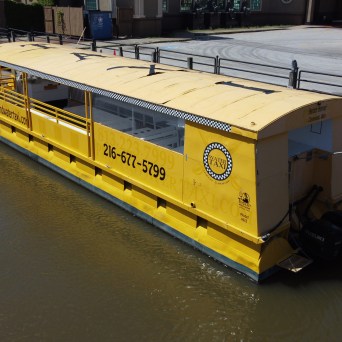 Yellow water taxi docked by a riverside walkway on a sunny day.