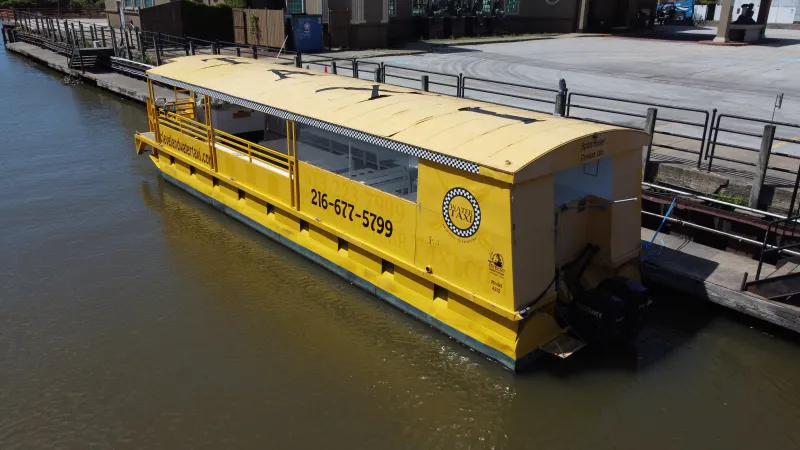 Yellow water taxi docked by a riverside walkway on a sunny day.