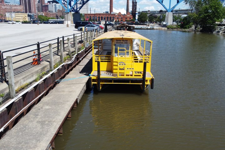Yellow boat docked on a river next to a concrete pier with buildings and a bridge in the background.