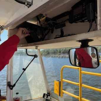 Person adjusting radio equipment on a boat with a lake view in the background.