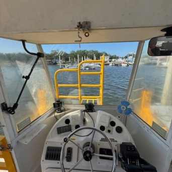 View from inside a boat cockpit with a steering wheel and controls, looking out at a marina.