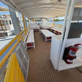 Open boat deck with yellow railings, wooden floor, benches, and a fire extinguisher mounted on a wall.