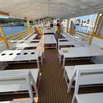 Open-air boat seating with white benches and tables, docked by a waterfront.
