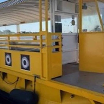 Yellow pontoon boat docked on a sunny day with water and trees in the background.