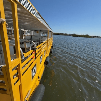 Yellow water taxi with checkered pattern docked on calm water under clear blue sky.