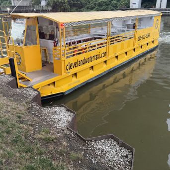 Yellow water taxi docked by a riverbank with a bridge in the background.