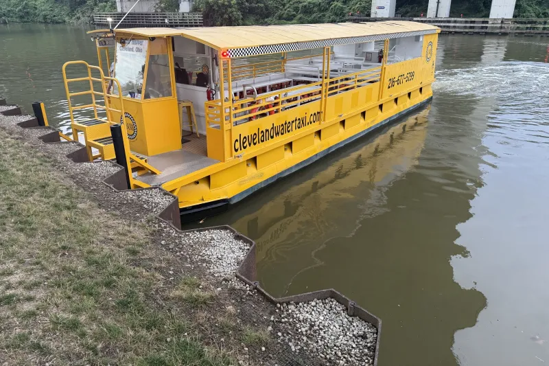 Yellow water taxi docked by a riverbank with a bridge in the background.