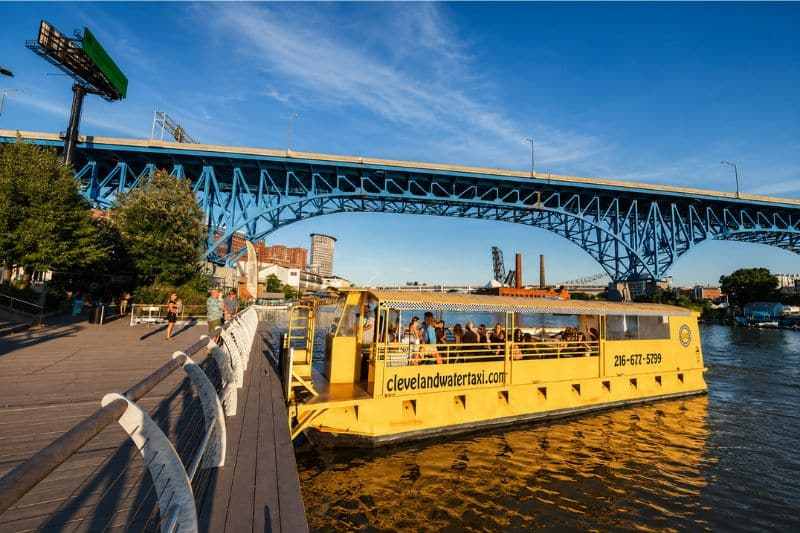 Yellow water taxi on the river near a blue bridge under a clear sky.